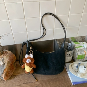 Detail of black suede crescent bag featuring a brown teddy bear charm on wooden table