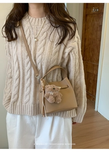 Chic beige bucket bag detail featuring a metal twist lock and a cute plush bear charm