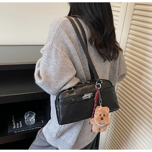 Detail of black rectangular shoulder bag with silver clasp and plush bear charm accent