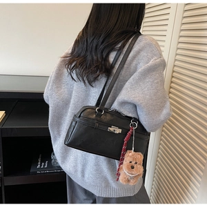 Detail of black leather shoulder bag with silver clasp and cute plush bear charm