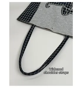 Détail des bretelles élargies et broderie Snoopy sur un sac fourre-tout gris