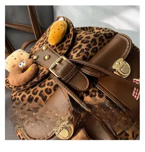 Close-up of leopard print backpack showing leather trim and plush charm accessories