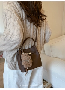 Detail of brown litchi leather bucket bag featuring a plush bear charm and metal lock