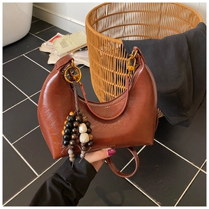 Gros plan du sac hobo marron vintage avec détails dorés et pompon en perles de bois