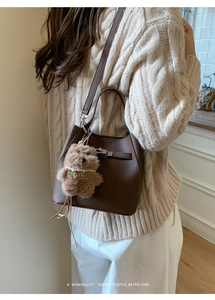 Close-up of brown pebbled leather bucket bag with twist lock and cute teddy bear charm