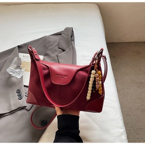 Detail of burgundy leather hobo bag with embossed logo and retro beaded charm accent
