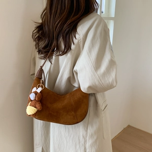 Detail view of brown suede crescent bag with a cute plush bear charm on the strap