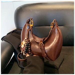 Détail du sac demi-lune marron foncé avec boucle dorée et pompon en perles de bois coloré