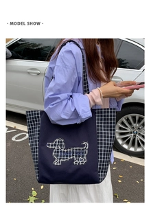 Détail du sac cabas en toile à carreaux avec broderie teckel porté par un mannequin en rue