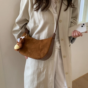 Close-up of brown suede crescent bag with a cute knit rabbit charm on a stylish model