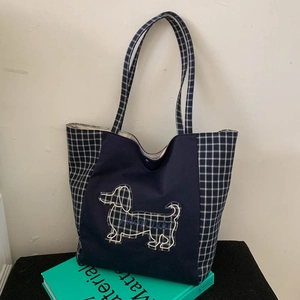 Détail de la broderie de teckel sur un sac cabas en toile bleue aux motifs à carreaux