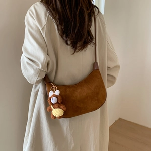 Detail view of brown suede half-moon shoulder bag with a cute teddy bear charm on model