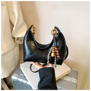 Détail du sac hobo en cuir verni noir avec logo doré et pendentif en perles