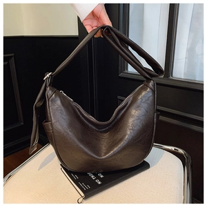 Detail of dark brown faux leather hobo bag with knotted wide strap on a white chair