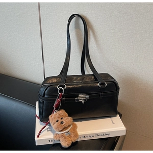 Detail of black leather Boston bag with silver lock and plush puppy charm on books