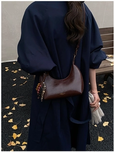 Détail du sac bandoulière demi-lune en cuir marron foncé avec pompon en perles
