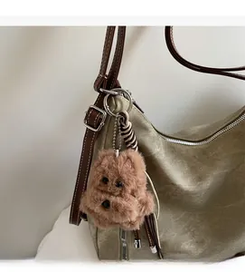 Detail view of a plush dog charm with metal lobster clasp on a khaki canvas tote bag