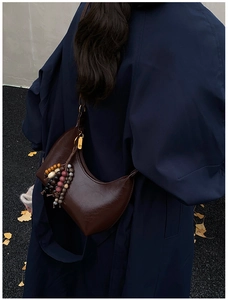 Détail du sac hobo marron avec pompon en perles de bois sur un manteau bleu marine