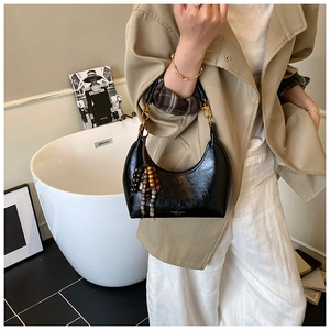 Détail d'un sac à bandoulière noir en forme de croissant avec pompon perlé et boucles dorées