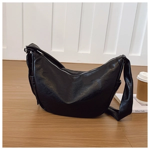 Close-up of black crescent hobo bag with silver zipper on a wooden floor