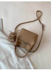 Macro view of tan lychee grain leather bucket bag with metal buckle and bear charm
