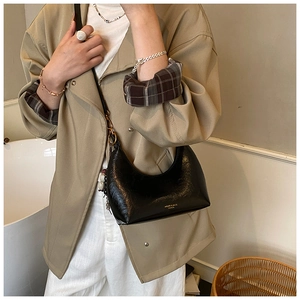 Détail du sac croissant noir verni avec finitions dorées porté par un mannequin