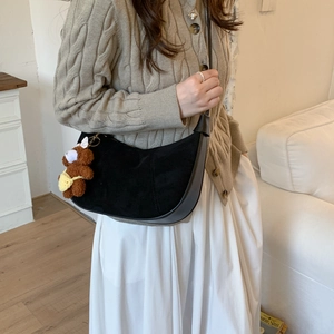 Detail shot of a black suede hobo bag with a cute bear charm on a model shoulder