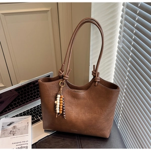 Close-up of brown faux leather tote bag with wooden bead tassel and knotted handle detail