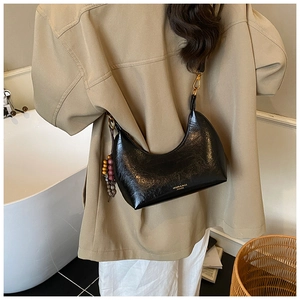 Détail d'un sac hobo demi-lune noir avec texture cirée et breloque à perles colorées et pompons