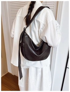 Detail of a dark brown crescent bag with leather pleated texture worn over a white shirt
