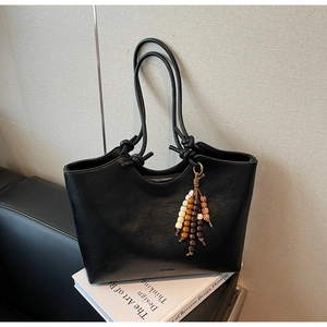 Detail view of a black tote bag with beaded charm and knot decoration on an open top