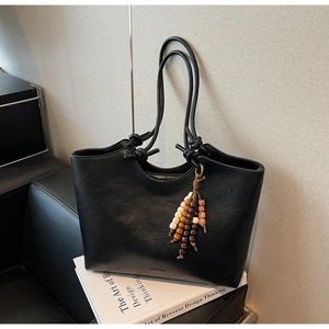 Detail of black tote bag featuring dual slim shoulder straps and colorful beaded tassel charm