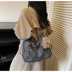 Detail of grey tote bag with side zipper pocket, leather strap and plush dog charm