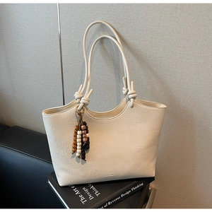 Detail of creamy white leather tote bag with knotted strap and beaded tassel on a book