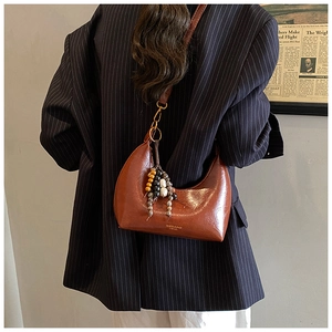 Détail d'un sac demi-lune marron avec pompon en perles et logo doré chic