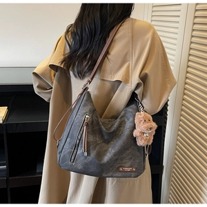 Detail of grey soft hobo tote bag with plush puppy pendant and brown leather shoulder strap
