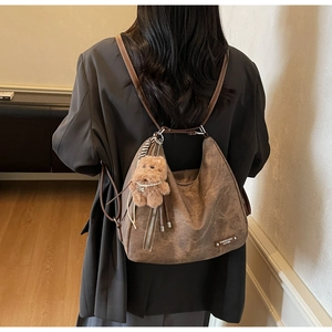 Detail of brown vintage hobo bag with teddy bear charm on model wearing grey blazer