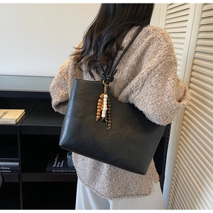 Detail of black matte leather tote bag featuring vintage wooden bead tassel ornament