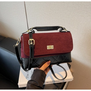 Detail der weinroten Wildlederklappe und schwarzen gesteppten Handtasche mit Goldschloss