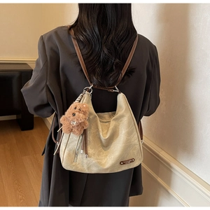 Detail view of beige pleated shoulder bag with brown strap and plush bear charm accent