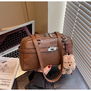 Detailed view of a brown vintage leather shoulder bag with a cute teddy bear charm