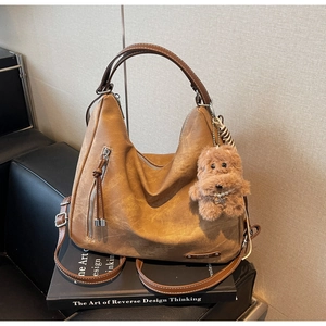 Detail of a brown vintage leather tote bag with a plush puppy charm on a book