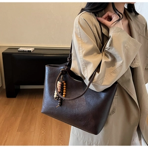 Close-up of vintage brown leather tote bag with retro wooden bead pendant detail