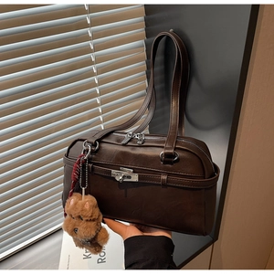 Close-up of deep brown Boston bag with metal lock and cute teddy bear pendant charm