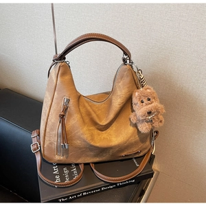 Detail of caramel hobo bag with fringe zipper, plush bear charm on art book