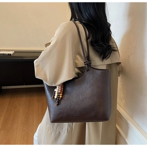 Close-up of a large dark brown tote bag with natural leather texture and bead tassel