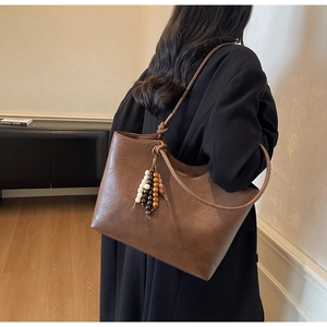 Detail of brown leather tote bag with vintage texture and colorful bead pendant