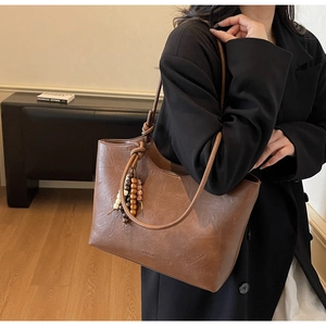 Detail of a dark brown vintage tote bag with wooden bead pendant and matte leather finish