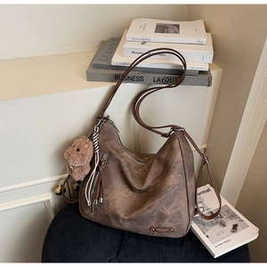 Close-up of vintage brown leather tote bag with plush charm on a textured seat