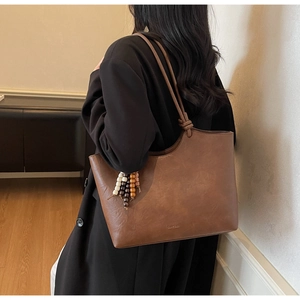 Detail of vintage brown tote bag showing leather texture and decorative beaded tassel